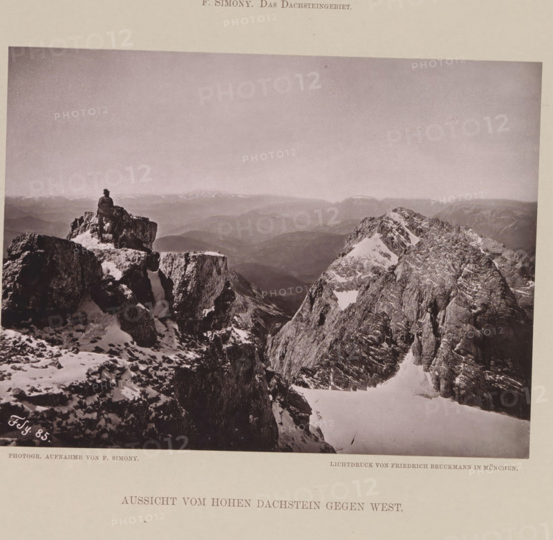 View from the Dachstein Mountains, Aussicht vom Hohen Dachstein gegen west, page, photomechanical print, number: 'XI.', photographer: Friedrich Simony, Dachstein (Salzburg), cliché maker: Friedrich Bruckmann, Vienna, publisher: Eduard Hölzel, 1885, Lower Austria, paper, collotype, photoprint, height 142 mm x width 191 mm, mountain-top, peak, A sepia-toned photograph showing a high mountain scene with jagged rocky peaks partially covered in snow, a person seated on a prominent rock outcrop near the left side facing the distant landscape, layered mountain ridges fading into the horizon under a vast pale sky, steep rock faces and snow-filled gullies in the foreground, and scattered patches of snow on the rocks.
