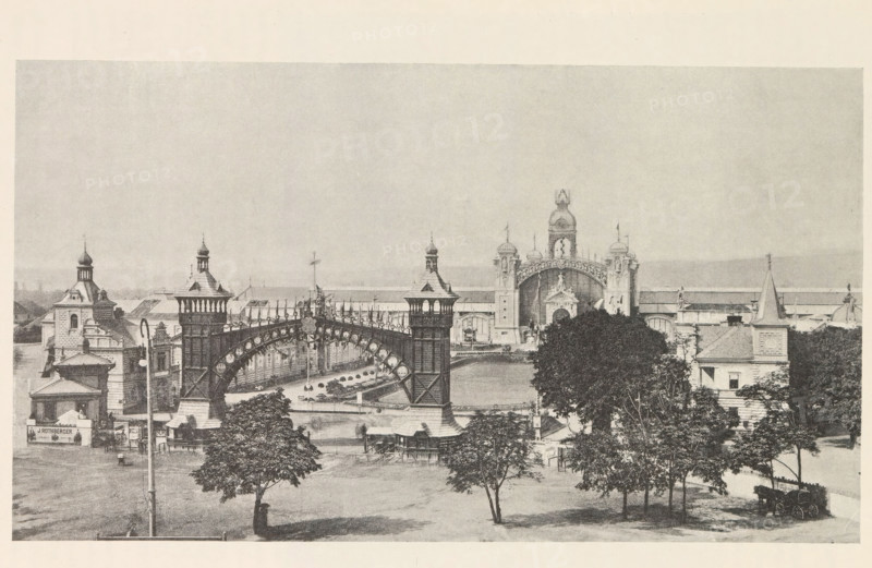 Pohled na výstavu od jihu v dobe zahájeni, View of the Výstavište in Prague, page, photomechanical print, Prague, cliché maker: Carl Bellmann, c. 1888 - in or before 1893, photographer, paper, autotypie, height 152 mm x width 264 mm, temporary exhibition, 'Salon', façade (of house or building), Výstavište, A wide view shows an ornate entrance complex with tall decorative towers and an arched iron bridge spanning between two larger towers, detailed with circular motifs and railings. In the foreground there are several trees with full canopies, a grassy area, and a few small structures and lampposts. Behind the bridge an elaborate central building features domed cupolas, sculptural decorations, and a large arched portal flanked by towers with ornamental tops. Flanking buildings with pitched roofs, turrets, and chimneys extend to either side, and a carriage sits near the lower right corner. The sky above is pale and empty.