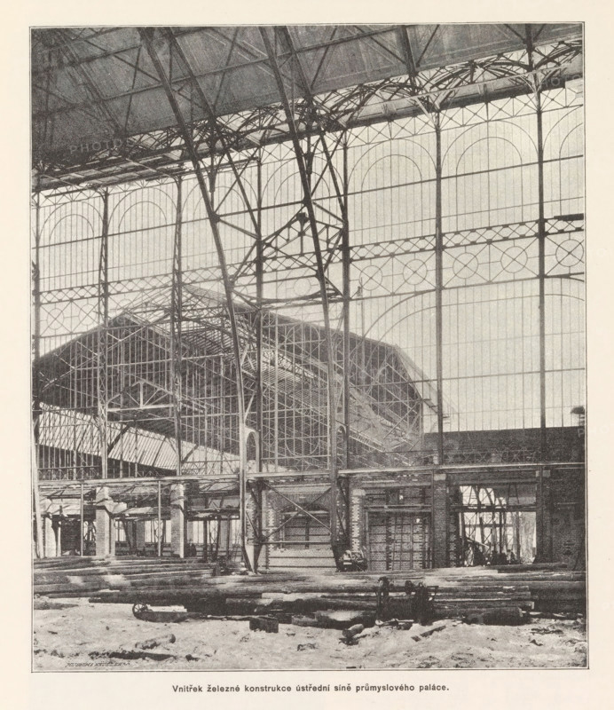 Vnitrek zelezné konstrukce ustredni sine prumysloveho paláce, Interior of the Industrial Palace under construction in Prague, page, photomechanical print, Výstavište, cliché maker: Carl Bellmann, Prague, c. 1888 - in or before 1893, photographer, paper, autotypie, height 220 mm x width 190 mm, building-site, A large interior space dominated by a tall iron framework and glass walls with arched window patterns, showing vertical and horizontal metal beams, lattice trusses, and curved supports; an elevated roof structure with visible rafters and intricate metalwork stretches across the top; beneath the iron skeleton there are platforms, scaffolding, and partial brick or stone walls with openings and columns; the floor area contains scattered long wooden beams and construction debris, and a small wheeled cart is visible among the materials; overall the scene shows an industrial building under construction with exposed structural elements and large glazed panels.