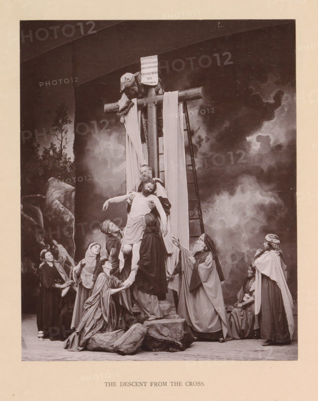 The descent from the cross, page, photomechanical print, inscription: 'Gemeinde Oberammergau Passionsspiel 1890', photographer: Carl Stockmann, Oberammergau, cliché maker: anonymous, c. 1885 - in or before 1890, Bavaria, paper, collotype, photoprint, height 218 mm x width 178 mm, group of actors, troupe, actors on the stage, descent from the cross: Christ is taken down from the cross, usually by Nicodemus and Joseph of Arimathaea who are standing on the ladders (both arms of Christ detached), A sepia-toned staged scene shows a group of robed figures gathered around a wooden cross set against a painted cloudy backdrop, with a ladder leaning against the cross and a cloth draped over the horizontal beam; a central bearded man supports the limp body of another man while several other figures reach up and cradle him, some kneeling and some standing, their garments flowing with folds and head coverings of varied styles; a small rocky foreground and scattered props sit at the base of the scen...