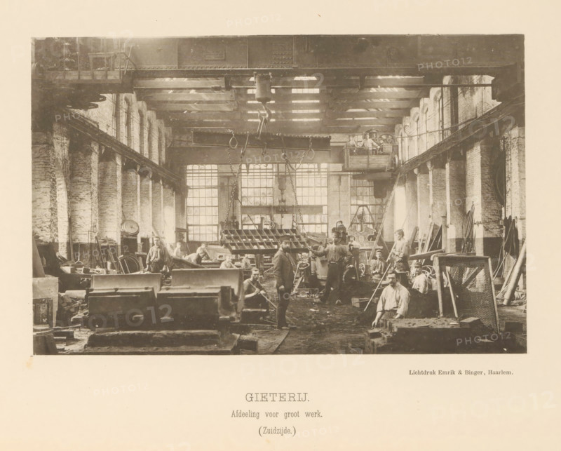 Foundry. Large-scale work department. (South side), Interior with employees of the foundry of the machine factory of Gebroeders Stork & Co, page, photomechanical print, number: 'No. 4.', Hengelo (Overijssel), maker: Emrik & Binger, Haarlem, c. 1884 - in or before 1894, photographer, paper, collotype, photogravure, height 131 mm x width 203 mm, factory-building, workshop, A wide interior view of a large industrial workshop with tall arched windows along both side walls, wooden roof beams and a large overhead crane with chains and hooks suspended above the workspace; numerous workers in period clothing stand and sit among heavy machinery, metal parts, tools, crates and workbenches scattered across the floor; a raised platform with additional workers and equipment is visible toward the back right, and ladders, racks and various long metal rods lean against the right wall; light filters through the windows creating bright rectangles on the back wall and work area.