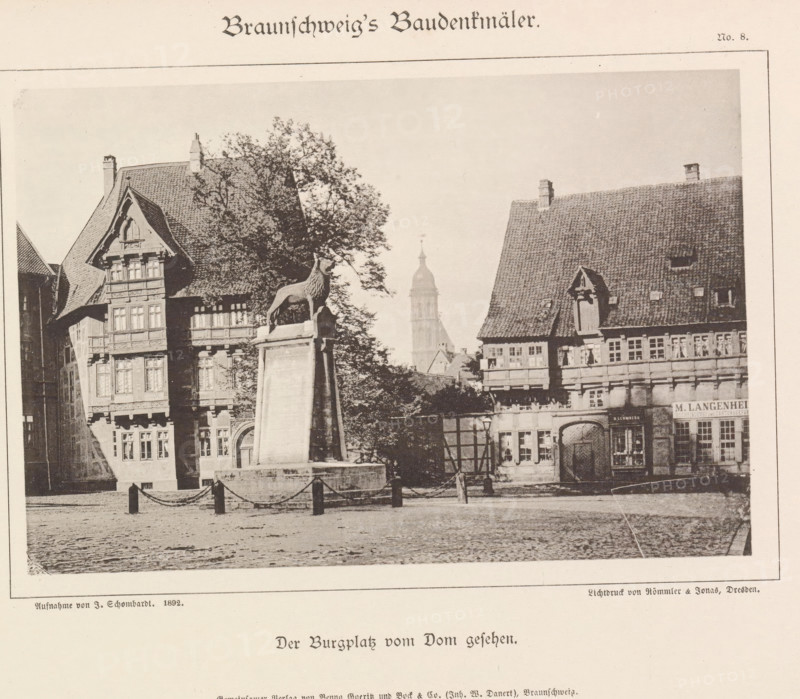 Der Burgplatz vom Dom gesehen, Burgplatz te Braunschweig, Braunschweig's Baudenkmäler, page, photomechanical print, number: 'No. 8.', photographer: J. Schombardt, Burgplatz (Braunschweig), cliché maker: Römmler & Jonas, Dresden, publisher: Benno und Wilhelm Danert Goeritz, Braunschweig, c. 1892, J. Schombardt, Römmler & Jonas, Benno und Wilhelm Danert Goeritz, photographer, cliché maker, publisher, Lower Saxony, Saxony, paper, collotype, photoprint, height 105 mm x width 160 mm, village square, Place, A sepia-toned scene of a town square showing ornate timber-framed buildings with steep tiled roofs and decorative facades, a tall tree partially obscuring one building, a stone pedestal topped by a sculpted animal figure in front of the tree, a cobbled ground in the foreground with short posts linked by chains, a narrow arched doorway and multiple windows on the buildings, a distant tower rising above the rooftops, and a lamppost near the base of the pedestal.