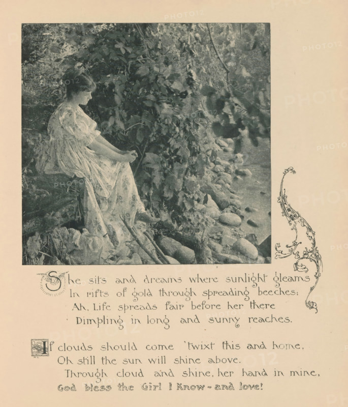Woman sitting on a waterfront with trees, page, photomechanical print, photographer: Mary Bartlett, United States of America, cliché maker: anonymous, c. 1884 - in or before 1894, North America, paper, photoaquatint, height 132 mm x width 136 mm, adolescent, young woman, maiden, forest, wood, river bank, A monochrome photograph shows a young woman seated on a rocky, leaf-strewn bank beside a body of water, wearing a flowing, patterned dress with puffed sleeves and holding her hands together in her lap, her head turned slightly downward and hair pulled back; dense foliage and overhanging branches fill the background and extend toward the water where smooth stones line the shoreline, and a decorative floral scroll appears at the edge of the page.