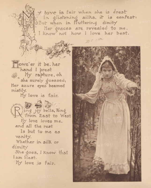 Portrait of an unknown girl with a white dress and a white bonnet in a garden, page, photomechanical print, photographer: Mary Bartlett, United States of America, clichémaker: anonymous, c. 1884 - in or before 1894, North America, paper, photoaquatint, height 169 mm x width 85 mm, girl (child between toddler and youth), dress, gown, A sepia-toned page shows an ornate decorative border and floral illustrations on the left and a tall rectangular photograph on the right of a young girl standing among foliage; she wears a light-colored long dress with ruffled trim and a bonnet with ties, her arms are extended outward with one hand touching a branch, and her expression is neutral while she looks toward the camera, with trees and leaves filling the background.
