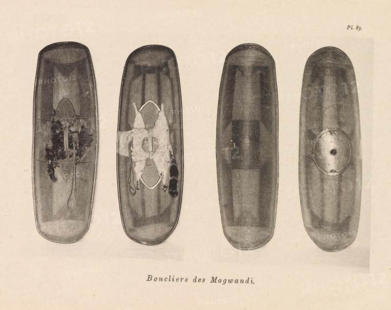 Boucliers des Mogwandi, Four shields of the Ngbandi, page, photomechanical print, number: 'Pl. 83.', photographer: Franz Thonner, cliché maker: Stengel & Markert, Dresden, 1896, Saxony, paper, collotype, photoprint, height 109 mm x width 161 mm, protective weapons: shield, Four elongated oval wooden shield-like objects are arranged horizontally across a pale background, each shown with a top-to-bottom orientation. The leftmost object has a dark textured surface with a central area showing rough, fibrous material and a looped cord hanging downward; the second from left has a similar textured surface with a patched, irregular cloth or hide affixed near its center and edges of frayed material extending from it. The third object from left appears smoother and darker with faint linear striations and a subtle central raised area, while the rightmost object shows concentric fine lines near its top and a round metal or disc-like plate attached off-center toward its lower half. The overall imag...
