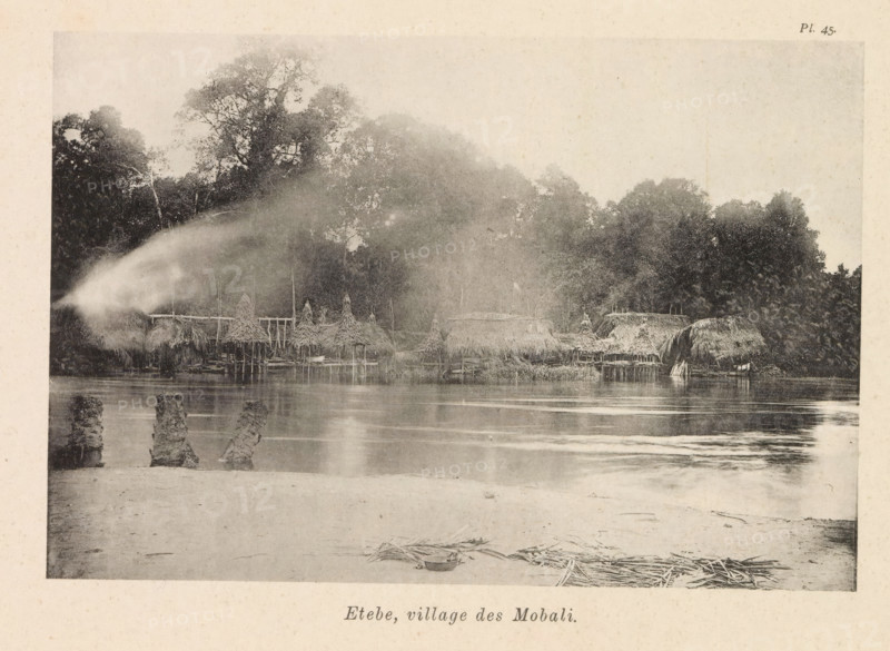 Etebe, village des Mobali, View of Etebe, page, photomechanical print, number: 'Pl. 45.', photographer: Franz Thonner, Congo (country), cliché maker: Stengel & Markert, Dresden, 1896, Saxony, paper, collotype, photoprint, height 110 mm x width 161 mm, city-view in general, 'veduta', façade (of house or building), A riverside scene shows a row of thatched huts and raised structures along the water's edge, with conical and rounded roofs made of straw or similar material and wooden stilts visible beneath some huts; dense trees and foliage rise behind the huts, forming a dark treeline with taller tree canopies toward the left; the river in front reflects the huts and trees with gentle ripples, and remnants of wooden posts or stumps project from the shallow water nearer the shore; a sandy foreground contains scattered bundles of reeds or straw and a shallow bowl or basin resting on the sand; a soft mist or spray drifts across the left side of the image, blurring part of the huts and trees.