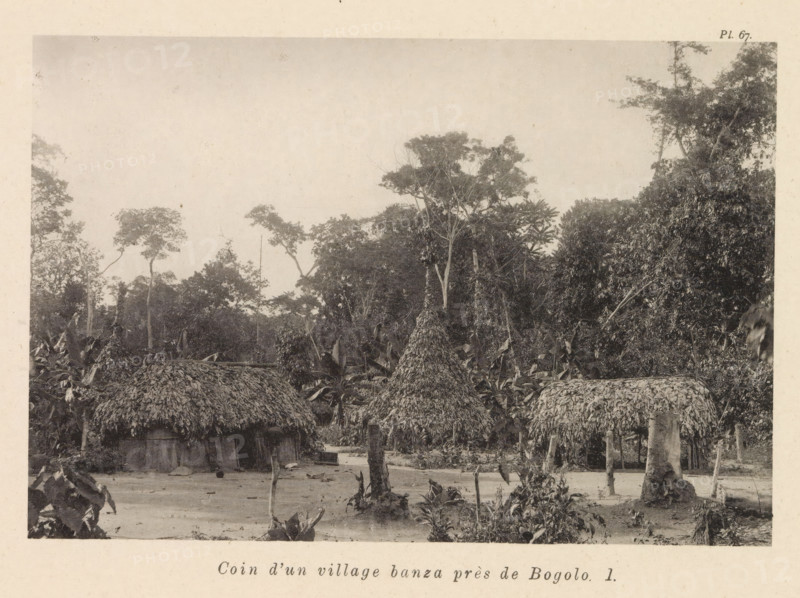 Coin d'un village banza près de Bogolo I, Houses in a Banza village near Bogolo, page, photomechanical print, number: 'Pl. 67.', photographer: Franz Thonner, Congo (country), cliché maker: Stengel & Markert, Dresden, 1896, Franz Thonner, Stengel & Markert, photographer, cliché maker, Saxony, paper, collotype, photoprint, height 108 mm x width 161 mm, housing, façade (of house or building), A sepia-toned scene showing a cluster of round thatched huts with conical roofs made of layered plant material, set on bare ground with scattered vegetation and small plants in the foreground; behind the huts a dense stand of tall trees with varied canopies rises, including slender trunks and broad leafy branches, with additional foliage and smaller plants filling the midground and edges of the image.