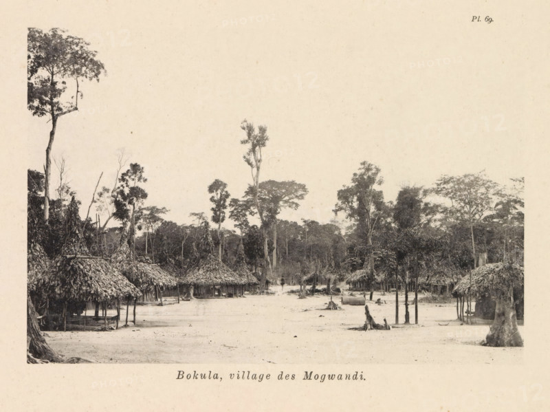 Houses in Bokula, Bokula, village des Mogwandi, page, photomechanical print, number: 'Pl. 69.', photographer: Franz Thonner, cliché maker: Stengel & Markert, Dresden, 1896, Saxony, paper, collotype, light printing, height 108 mm x width 161 mm, housing, façade (of house or building), A wide clearing bordered by dense trees fills the scene, with a series of thatched huts arranged along the edge of the open ground. The huts have conical, textured roofs made of layered plant material and open-sided walls supported by vertical posts, some showing raised platforms beneath the roofs. Scattered tree stumps and upright trunks rise from the sandy or bare earth of the clearing, while taller trees with leafy canopies frame the background and tower above the huts. The overall image is monochrome and shows a natural forest edge transitioning into a simple village area with visible trunks, branches, and clustered foliage.