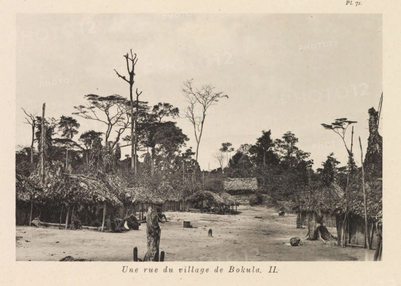 View of a street in Bokula, Une rue du village de Bokula II, page, photomechanical print, number: 'Pl. 71.', photographer: Franz Thonner, Bokula, cliché maker: Stengel & Markert, Dresden, 1896, Saxony, paper, collotype, photoprint, height 108 mm x width 161 mm, street, housing, A wide dirt clearing bordered by clusters of thatched huts with roofs made of layered vegetation and simple wooden supports, some huts arranged along a faint path leading toward a denser treeline; scattered tree stumps and upright wooden posts rise from the ground, and rough logs and cylindrical objects lie on the clearing; in the background thin tall trees with sparse branches and broader canopied trees form a forest edge that fills the upper half of the scene under a pale sky.