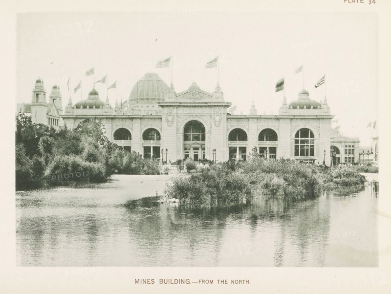 View of the building for mines and mining, designed by Solon Spencer Beman at the World's Columbian Exposition in Chicago in 1893, Mines Building.- From the north, page, photomechanical print, number: 'Plate 34', photographer: Charles Dudley Arnold, Chicago, photographer: HD Higinbotham, clichémaker: anonymous, 1893, Charles Dudley Arnold, HD Higinbotham, photographer, clichémaker, North America, Illinois, paper, collotype, photogravure, height 134 mm x width 191 mm, world fair, world exhibition, World's Columbian Exposition, A large classical building with a central dome and flanking smaller domes sits behind a body of water and dense shrubbery, showing a symmetrical façade with arched windows and ornate architectural detailing, flagpoles with flags flying atop the roofline, lamp posts and small groups of people visible near the entrance, and reflected ripples of the structure and vegetation in the calm water in the foreground.