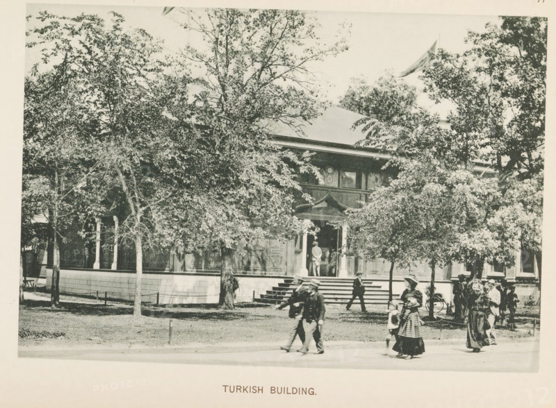 Pavilion of Turkey at the World's Columbian Exposition in Chicago in 1893, Turkish Building, page, photomechanical print, number: 'Plate 77', photographer: Charles Dudley Arnold, Chicago, photographer: HD Higinbotham, cliché maker: anonymous, 1893, Charles Dudley Arnold, HD Higinbotham, photographer, cliché maker, North America, Illinois, paper, collotype, light printing, height 130 mm x width 190 mm, world fair, world exhibition, World's Columbian Exposition, A large building partially obscured by numerous leafy trees sits behind a low wall with a series of steps leading up to a covered entrance; the building has ornate woodwork around the doorway and windowed panels along its facade, with a person standing in the entranceway. In the foreground several people walk along a path or street, including adults wearing long coats and hats and a child in a patterned dress, while others stand near the steps and a bicycle is visible near a group to the right.