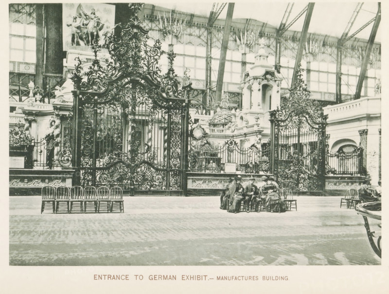 Entrance gates to the German exhibition during the World's Columbian Exposition in Chicago in 1893, Entrance to German exhibit.- Manufactures Building, page, photomechanical print, number: 'Plate 8', photographer: Charles Dudley Arnold, Chicago, photographer: HD Higinbotham, cliché maker: anonymous, 1893, Charles Dudley Arnold, HD Higinbotham, photographer, cliché maker, North America, Illinois, paper, collotype, photoprint, height 134 mm x width 190 mm, world fair, world exhibition, World's Columbian Exposition, An ornate wrought iron gate with intricate scrollwork and decorative motifs fills the midground, flanked by sculpted stone structures and architectural embellishments with carved figures and ornamental domes behind it, set within a large glass and iron exhibition hall whose framework and high windows are visible above; a row of wooden chairs is arranged in front of the gate on a patterned floor, and a small group of people in period clothing sit on chairs near the center, whil...