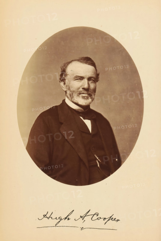 Portrait of Hugh A. Cooper, Hugh A. Cooper, photograph, page, photographer: Bendann Bros., c. 1866 - in or before 1871, paper, albumen print, height 137 mm x width 110 mm, Person, historical persons, An oval sepia-toned portrait of an older man shown from the chest up, seated and wearing a dark suit jacket, waistcoat, and a bow tie with a light shirt collar visible, his face framed by short hair and a trimmed beard and mustache, with a neutral background inside the oval and a light creamy border surrounding the portrait.