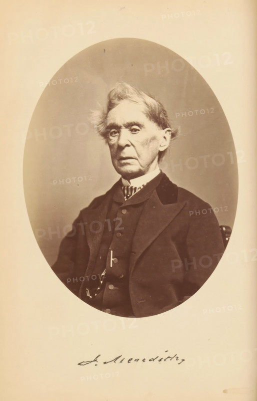 J. Meredith, Portrait of Jonathan Meredith, photograph, page, photographer: Bendann Bros., c. 1866 - in or before 1871, paper, albumen print, height 148 mm x width 114 mm, Person, Jonathan Meredith, historical persons, An oval-framed sepia photograph of an elderly man shown from the chest up wearing a dark suit jacket, vest, and a high-collared shirt with a patterned neckpiece, his hair light and tousled, his face long with deep-set eyes and prominent cheekbones, and the image set against a plain light background with a wide margin around the oval.