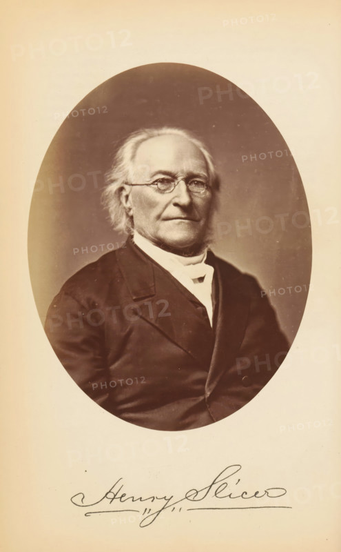 Henry Slicer, Portrait of Henry Slicer, photograph, page, photographer: Bendann Bros., c. 1866 - in or before 1871, paper, albumen print, height 147 mm x width 115 mm, Person, historical persons, An oval sepia photograph of an older man shown from the chest up, with light hair brushed back and sideburns, wearing round eyeglasses and a dark suit jacket over a white high-collared shirt and cravat, set against a softly shaded background and mounted on a pale page.