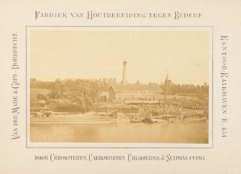 View of the Van der Made & Gips factory on the Oude Maas in Dordrecht, Factory for Wood Preservation against Decay, photograph, page, View of the wood preservation factory of Van der Made & Gips on the Oude Maas, at the entrance to the Papegat, in Dordrecht., inscription: 'Van der Made & Gips - Dordrecht., Office: Kalkhaven E. 451., by Creosoting, Carbonizing, Zinc Chlorocarbon & Sulphas-Cupri', Kalkhaven (Dordrecht), c. 1867 - in or before 1872, photographer, Dordrecht, paper, albumen print, height 88 mm x width 141 mm, Photo opposite title page., factory-building, Oude Maas, A sepia-toned photograph framed by a pale border shows a waterfront scene with a long, low building topped by a tall chimney rising behind it, surrounded by stacks of logs and timber. Several small boats and larger vessels sit at the water's edge, some with masts and rigging, and people are visible working on the docks and among the stacks. Trees form a treeline behind the building, and the water in the foregroun...
