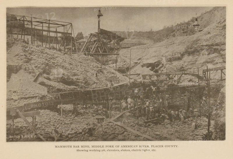 Mammoth Bar Mine, Middle Fork of American River, Placer County, View of Mammoth Bar Mine in Placer County, California, page, photomechanical print, inscription: 'Showing working pit, elevators, sluices, electric lights, etc.', maker: Britton & Rey, c. 1885 - in or before 1890, North America, paper, collotype, photoprint, height 112 mm x width 184 mm, mine, miner, A sepia-toned photograph shows a rugged excavation site with steep dirt and rock slopes and scattered rounded stones across the ground. Wooden scaffolding and elevated walkways cross the scene, with slanted beams and ladders connecting different levels. A tall pole topped with a bell-like structure rises above the central area, and another similar structure stands on a distant hillside. Workers wearing light clothing and hats are clustered along the lower platforms and among the rocks, with some figures on the elevated walkways. Crude wooden chutes and troughs run across the site, and piles of rocks and earth are heaped near t...