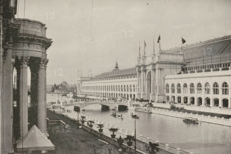 Manufacturer's buildings, world's fair, Chicago, page, photomechanical print, photographer: Charles Dudley Arnold, cliché maker: Benedict & Co., Geo. H., 1893, North America, Illinois, paper, autotypie, height 116 mm x width 173 mm, world fair, world exhibition, A riverside scene showing a large classical building with arched windows and tall decorative columns, a grand entrance with ornate towers and flags on top, and a long roof with a row of railings; in front of the building a curved bridge spans the water, several small rowboats and a larger boat float on the river, and promenades with lamp posts and potted plants run along the waterfront; on the left foreground a portion of another columned structure is visible with a tented canopy below and sculptural details on the column capitals, while distant buildings and trees appear along the far bank beneath an open sky.