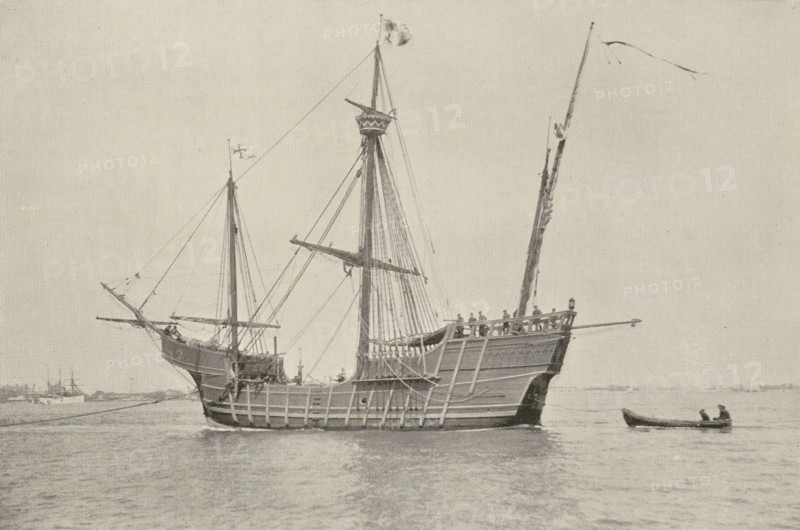 The 'Santa Maria', page, photomechanical print, photographer: J. Byron, cliché maker: Andrews & Son Co., J., c. 1888 - in or before 1893, paper, autotypie, height 108 mm x width 163 mm, ships (in general), A large wooden sailing ship with tall masts and rigging floats on calm water, its hull showing visible planking and a raised stern with a railing where several small figures stand, a smaller boat with two seated figures is alongside, flags fly from the mastheads and spars, rigging lines run between masts and down to the deck, and distant low shoreline and additional ships are visible on the horizon under a pale sky.