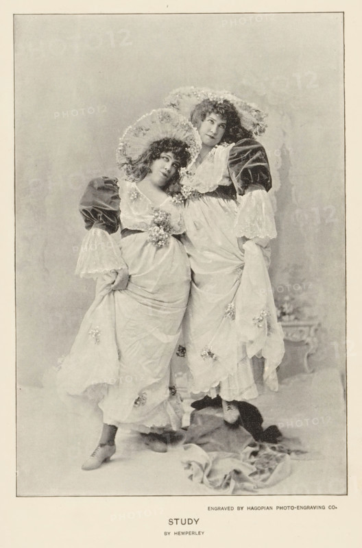 Study, page, photomechanical print, photographer: Hemperley, cliché maker: Hagopian Photo-Engraving Co., c. 1890 - in or before 1895, paper, autotype, height 159 mm x width 108 mm, adult woman, A sepia-toned photograph of two women standing close together wearing flowing light-colored dresses with floral embellishments and large ruffled sleeves, each holding up part of her skirt to reveal lace-trimmed underskirts and heeled shoes, both wearing wide brimmed hats decorated with flowers and looking slightly upward and to the side, one woman leaning her head toward the other, a draped fabric lying on the floor near their feet, and a plain mottled backdrop framed by a narrow border.