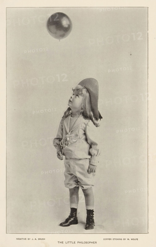 The little philosopher, page, photomechanical print, photographer: JA Brush, cliché maker: M. Wolfe, c. 1890 - in or before 1895, paper, autotypie, height 181 mm x width 113 mm, child, (flying a) gas balloon, A young child stands facing slightly sideways, wearing a loose long-sleeved top with a decorative element at the front, knee-length baggy shorts, and lace-up boots with socks; the child has shoulder-length wavy hair and wears a floppy hat tilted back while looking upward toward a round balloon floating above, against a plain light background.