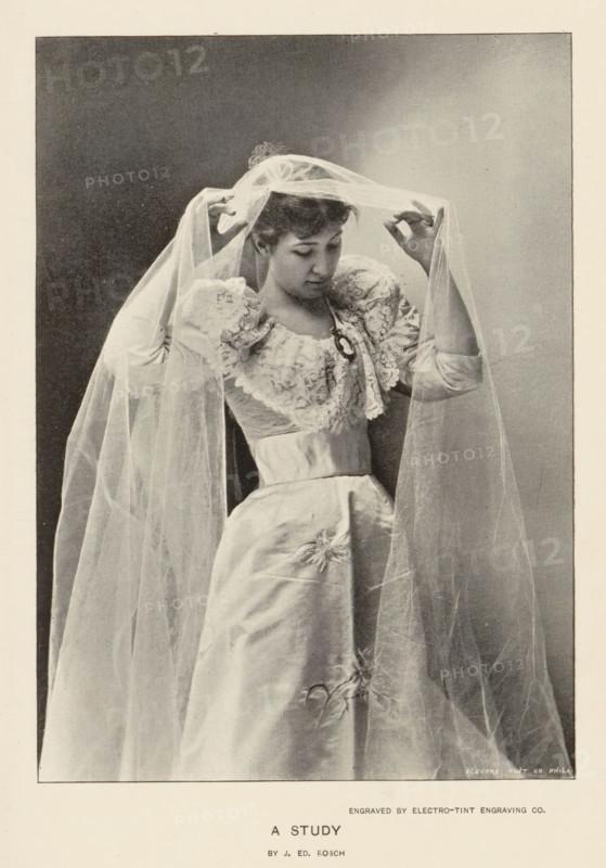A study, page, photomechanical print, photographer: J. Ed. Rosch, cliché maker: Electro-Tint Engraving Co., c. 1890 - in or before 1895, paper, autotypie, height 150 mm x width 108 mm, bride (in wedding dress), A woman wearing a formal gown with puffed sleeves and decorative lace on the bodice is shown adjusting a long translucent veil draped over her head and shoulders, her gaze directed downward, one hand lifting the veil near her forehead and the other holding it at the side, the skirt of the gown falling smoothly with a subtle floral embellishment, and a plain dark background framed within a lighter border.