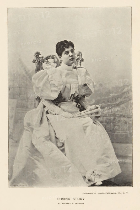 Posing study, page, photomechanical print, photographer: McCrary & Branson, cliché maker: Photo-Engraving Co., New York (city), c. 1890 - in or before 1895, North America, paper, autotype, height 153 mm x width 101 mm, adult woman, A black and white photograph shows a seated woman wearing a voluminous light-colored dress with puffed sleeves and a high neckline; she holds a folded fan in her gloved hands which rest in her lap. Her dark hair is short and styled close to her head, and she gazes slightly upward. The chair behind her has an ornate carved back with decorative scrollwork. The lower part of the image shows the full sweep of her dress draped over the seat and floor, and the background is a plain, softly textured backdrop.