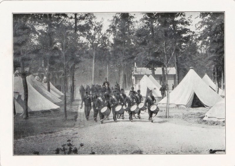 Soldiers marching into a tent camp, page, photomechanical print, photographer: Maurice Bucquet, Paris, cliché maker: anonymous, c. 1893 - in or before 1898, paper, autotypie, height 106 mm x width 159 mm, private soldier, (military) camp with tents, troop movements, transportation, A faded black and white photograph shows a row of canvas tents pitched among tall, slender trees in a wooded area, with a clearer cluster of larger tents on the right and smaller tents on the left; a group of uniformed men marches along a dirt path in the foreground, several carrying drums at waist level, others carrying long poles or marching behind them; in the background a small wooden building with a pitched roof stands between the trees, and figures can be seen near some tent entrances; the scene is framed by a wide white border.