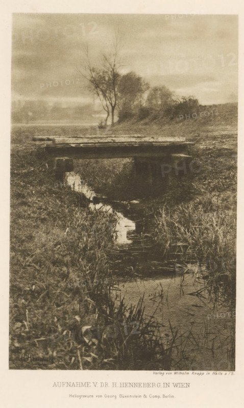 Bridge over a ditch, page, photomechanical print, photographer: Hugo Henneberg, Vienna, cliché maker: Büxenstein & Comp., Georg, Berlin, printer (person): Wilhelm Knapp Verlag, Halle an der Saale, c. 1893 - in or before 1898, printer (person), Lower Austria, Saxony-Anhalt, paper, photoaquatint, height 177 mm x width 112 mm, Print after page 192., brook, bridge, A sepia-toned photograph shows a narrow stream bordered by tall grasses winding toward the foreground, a simple wooden footbridge spanning the stream near the middle of the image, and a cluster of leafless and sparse trees on a low rise in the background beneath a cloudy sky.