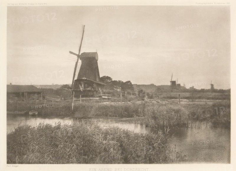Landscape with windmills near Dordrecht, Ein Abend bei Dordrecht, page, photomechanical print, Sawmills on the Noordendijk in Dordrecht. From left to right: De Jager, De Windhond and De Duinen, all three paltrok mills. The mill furthest right is the sawmill De Nachtegaal., photographer: Karl Greger, Dordrecht, clichémaker: anonymous, publisher: Wilhelm Knapp Verlag, Halle an der Saale, c. 1896 - in or before 1901, Saxony-Anhalt, paper, photoaquatint, height 155 mm x width 219 mm, behind semi-transparent cover with advertising message., windmill in landscape, A sepia-toned landscape showing a large traditional windmill near the center with one of its sails angled diagonally, smaller buildings clustered around its base, grassy marshland and a body of water in the foreground reflecting the scene, and additional distant windmills and low structures along the horizon under a broad, lightly textured sky.