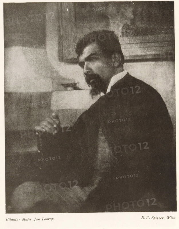 Bildnis: Maler Jan Toorop, Portrait of Jan Toorop, page, photomechanical print, monogram: 'LEIPZIG, S G', photographer: Friedrich Victor Spitzer, cliché maker: unknown, c. 1898 - in or before 1903, paper, autotypie, height 172 mm x width 140 mm, Person, Jan Toorop, historical persons, A monochrome portrait of a seated man shown from the side and slightly turned toward the viewer, with dark hair and a pointed beard, wearing a dark jacket and a light-colored collar, one hand resting on the arm of the chair and a relaxed posture, a framed rectangular object on the wall behind him and a light-toned rectangular surface at mid-height in the background, soft grainy texture across the image and a high-contrast tonal range.
