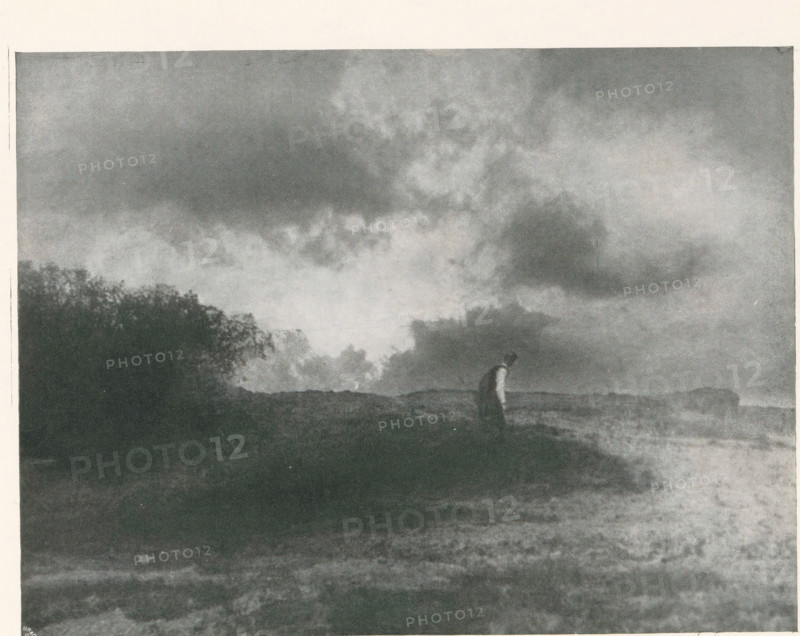 Man in a landscape, page, photomechanical print, photographer: Scholz, Th. & R., cliché maker: Meisenbach, Riffarth & Cie. (possibly), Berlin, c. 1898 - in or before 1903, paper, autotypie, height 139 mm x width 184 mm, Print on third unnumbered page after page 234., landscapes, adult man, A grainy black and white scene showing a wide sky filled with large, textured clouds above a dark landscape; near the horizon a solitary figure stands with a slightly bent posture wearing a darker outfit against a lighter background; to one side a dense cluster of foliage or trees creates a silhouette that contrasts with the open expanse, and the foreground shows uneven ground with varied tones and subtle texture.