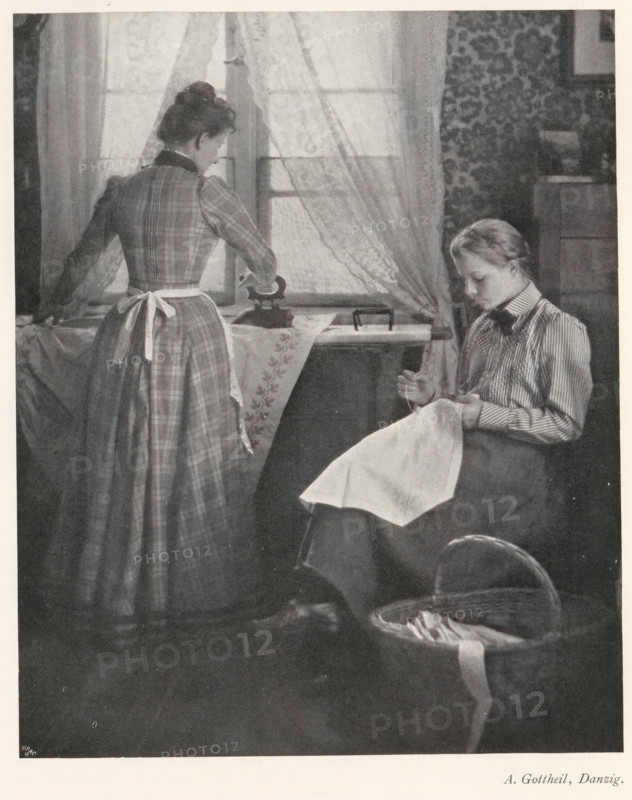 Woman ironing and a woman working with needles, page, photomechanical print, photographer: Albert Gottheil, cliché maker: Meisenbach, Riffarth & Cie. (possibly), Berlin, c. 1898 - in or before 1903, paper, autotypie, height 177 mm x width 144 mm, Print on second unnumbered page after page XI., sewing, ironing, A grayscale scene shows two women in a domestic interior near a window with sheer curtains; one woman stands with her back mostly to the viewer wearing a long plaid dress and a tied apron, her hair pulled up, and she has one hand on an iron placed on a covered table; the other woman sits to the right facing slightly downward, wearing a striped blouse and a dark skirt, holding a piece of cloth in her lap and appearing focused on it; a patterned wallpaper panel is visible behind the seated woman, a wooden cabinet edge appears nearby, and a woven basket with fabric and a long ribbon rests on the floor in the foreground.