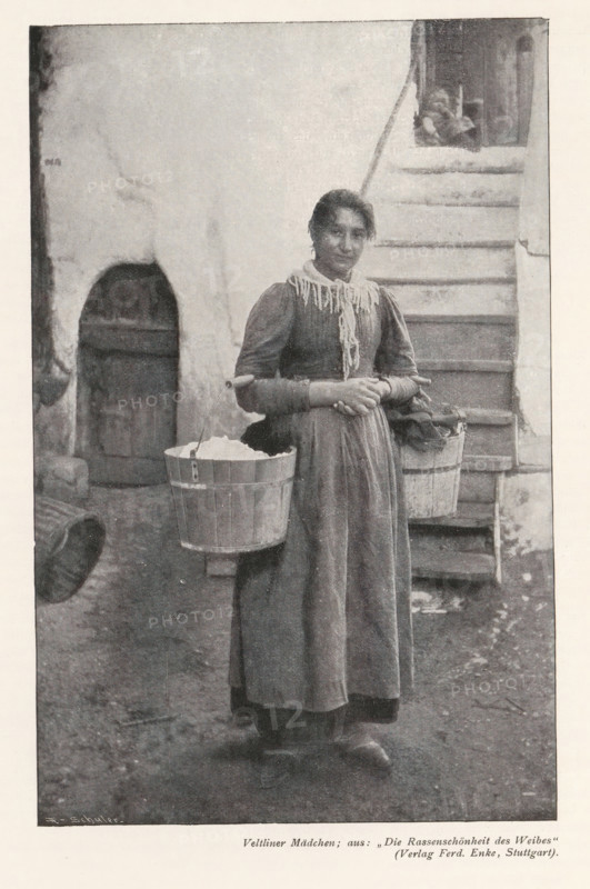 Portrait of an unknown girl with two buckets of laundry, Veltliner Mädchen, aus: 'Die Rassenschönheit des Weibes', (Verlag Ferd. Enke, Stuttgart), page, photomechanical print, photographer: A. Schuler, cliché maker: anonymous, c. 1898 - in or before 1903, paper, autotypie, height 177 mm x width 114 mm, historical persons not known by name - BB - woman, laundering, A young woman stands outdoors in front of a set of worn steps and a textured wall, wearing a long dress with a high neckline and a fringed scarf around her shoulders, her hair pulled back, hands clasped at her waist; she carries two wooden buckets suspended from a yoke across her shoulders, one bucket appearing filled with a light-colored material, while the other holds fabric; to the left of her is an arched doorway set into the wall and part of a large rounded object is visible on the ground; the ground beneath her is uneven and the overall image has a grainy, monochrome appearance.
