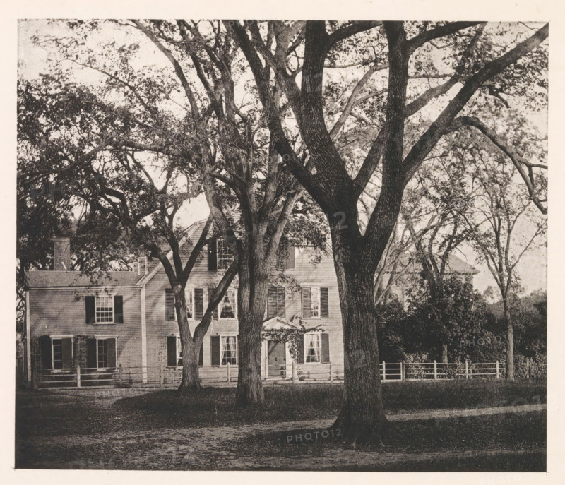 View of the home of Oliver Wendell Holmes Sr. in Cambridge, page, photomechanical print, photographer: William James Stillman, Cambridge (MA), cliché maker: anonymous, United States of America, c. 1866 - in or before 1876, North America, Massachusetts, paper, collotype, photoprint, height 148 mm x width 175 mm, Print opposite frontispiece., housing, façade (of house or building), A front view of a two-story house partially obscured by large trees with thick trunks and spreading branches, the house has multiple windows with shutters and a visible doorway with a small pediment, a wooden fence runs along the front yard, dense foliage and tree canopies fill the upper portion of the image, and the foreground shows a shaded grassy area and a dirt path.