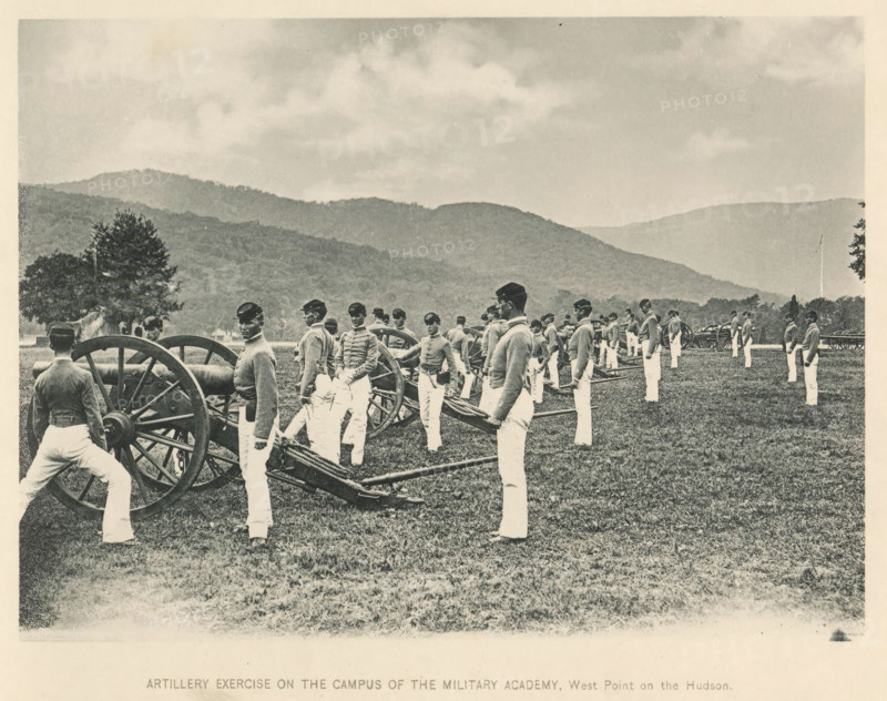 Artillery exercise on the campus of the Military Academy, West Point on the Hudson, Exercise with cannons at the United States Military Academy at West Point, page, photomechanical print, West Point, c. 1883 - in or before 1893, North America, paper, collotype, photoprint, height 140 mm x width 190 mm, firearms: cannon, military academy, A sepia-toned outdoor scene shows uniformed men standing beside large wheeled cannons on a grassy field with rolling tree-covered hills in the background and a cloudy sky above; the men wear dark caps and lighter jackets with light-colored trousers and are positioned in a line near the artillery pieces while trees appear at the edges of the field.