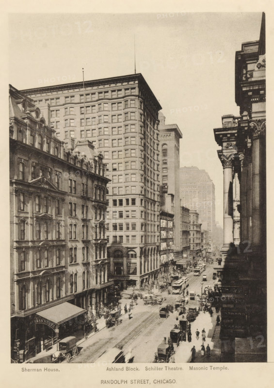 Randolph Street, Chicago, View of Randolph Street in Chicago, page, photomechanical print, inscription: 'Sherman House. Ashland Block. Schiller Theatre. Masonic Temple.', 1893, North America, Illinois, paper, collotype, photoprint, height 191 mm x width 140 mm, street, A vertically oriented sepia-toned photograph shows a busy city street flanked by tall multi-story buildings with ornate facades and rows of windows, the left side featuring a building with decorative roofline elements and the center dominated by a taller, rectangular structure with many evenly spaced windows, while the right foreground displays a classical building with large columns and ornate capitals; the street below is filled with horse-drawn carriages, early motor vehicles, streetcars, and numerous pedestrians moving along sidewalks and crossing the roadway, with awnings over some storefronts and smaller buildings receding into the distance beneath a pale sky.