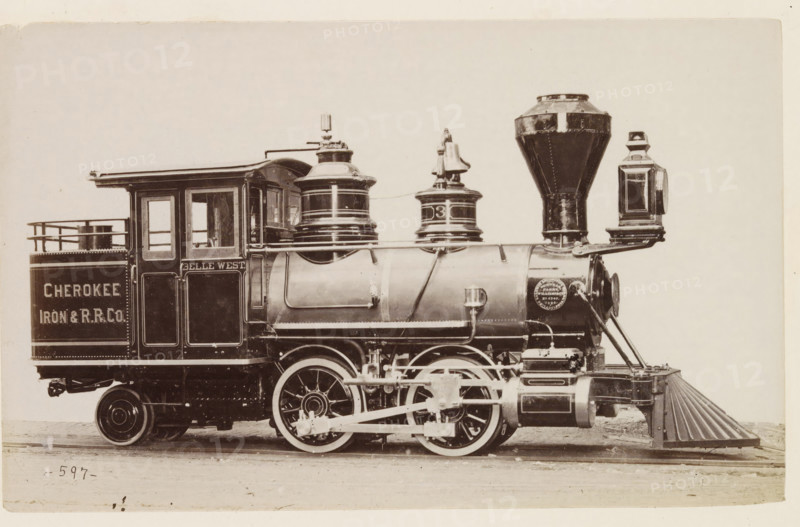 American steam locomotive, photograph, page, number: '597', United States of America, c. 1871 - in or before 1881, photographer, North America, paper, albumen print, height 125 mm x width 200 mm, Photo on page 128., steam locomotive, A sepia-toned side view of a vintage steam locomotive showing a cab with windows and a small railing, a cylindrical boiler with domed fittings and a tall tapered smokestack, a large headlamp mounted near the front, and a cowcatcher at the lower front; visible running gear includes large spoked driving wheels, connecting rods, and mechanical linkages; the locomotive has decorative trim and rivets, and there is a circular medallion-like plate on the boiler; the scene is framed against a plain light background and the train rests on rails with a ground surface beneath.