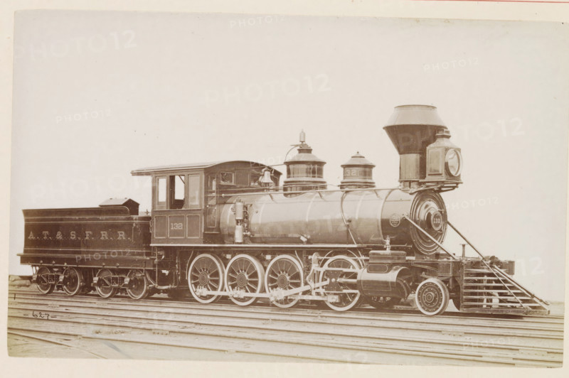 American freight steam locomotive, photograph, page, number: '627', United States of America, c. 1871 - in or before 1881, photographer, North America, paper, albumen print, height 123 mm x width 198 mm, Photo on page 104., steam locomotive, A sepia-toned side view of a steam locomotive and its tender resting on railroad tracks, showing the engine's large driving wheels with visible spokes, connecting rods, and mechanical linkages, a cylindrical boiler with domed steam domes and a bell mounted near the cab, a square cab with window openings, a tall tapered smokestack and a large rectangular headlight box at the front, and the tender behind the cab with a sloped top and visible wheelsets.