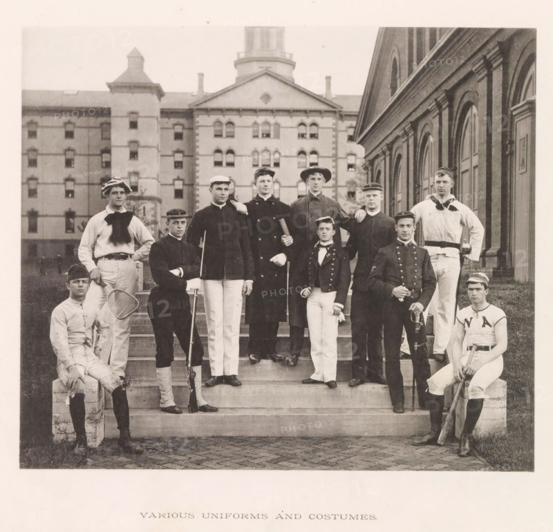 Various uniforms and costumes, photograph, page, photographer: Edward H. Hart, United States Naval Academy, cliché maker: The Photo-gravure Co., New York (city), c. 1885 - in or before 1890, North America, Maryland, Annapolis, paper, collotype, photoprint, height 180 mm x width 210 mm, officer, (military) uniforms, anonymous historical persons depicted in a group, in a group-portrait, A group of men posed on outdoor stone steps in front of a large brick building with arched windows, the men wearing a variety of dark jackets, light trousers, hats, and caps, with some holding sporting equipment like a tennis racket, a long wooden bat, and a rifle, and two men seated at the lower corners while others stand on the steps, the background showing a multi-story masonry building with many windows and a tower.