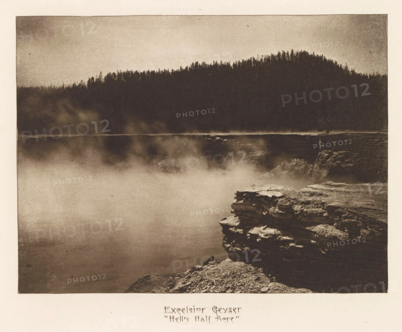 Excelsior Geyser 'Hell's Half Acre', page, photomechanical print, photographer: Frank Jay Haynes, Yellowstone National Park, cliché maker: The Photo-gravure Co., New York (city), c. 1882 - in or before 1887, Frank Jay Haynes, The Photo-gravure Co., photographer, cliché maker, North America, paper, photoaquatint, height 164 mm x width 220 mm, hot spring, geyser, Excelsior Geyser, A sepia-toned photograph showing a misty expanse of water in the foreground with rising steam or fog, a rocky cliff edge in the lower right with layered rock formations, and a dark tree-covered ridge silhouette across the upper portion of the image.