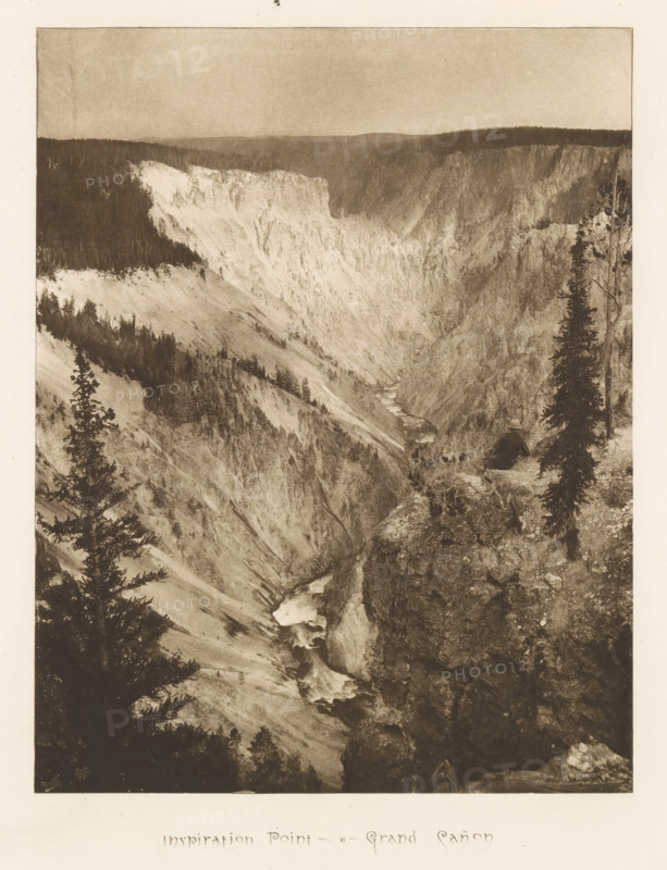 Inspiration point - Grand Cañon, page, photomechanical print, photographer: Frank Jay Haynes, Yellowstone National Park, cliché maker: The Photo-gravure Co., New York (city), c. 1882 - in or before 1887, North America, paper, photoaquatint, height 214 mm x width 166 mm, ravine, chasm, abyss, canyon, Grand Canyon (Yellowstone National Park), A sepia-toned photograph of a deep rocky canyon with steep light-colored cliffs and darker forested rimlines, a winding river flowing through the canyon with visible cascades and white water, rugged foreground rocks and a narrow ledge with sparse vegetation, several tall conifer trees framing the scene on the left and right, distant hazy hills forming the horizon under a muted sky.
