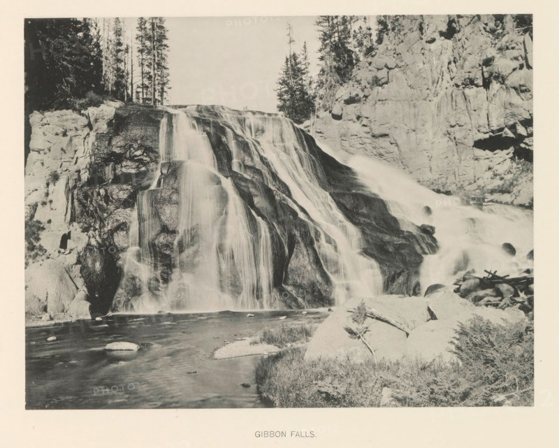 Gibbon Falls, page, photomechanical print, photographer: Frank Jay Haynes, Yellowstone National Park, cliché maker: The Photo-gravure Co., New York (city), c. 1886 - in or before 1891, North America, paper, collotype, photoprint, height 165 mm x width 216 mm, river, A wide waterfall cascades over layered rock ledges, the water appearing smooth as it flows down dark, rounded stones into a river below; steep rocky cliffs flank the falls on both sides, and tall, slender trees rise above the cliff edge at the top; in the foreground a rocky riverbank with scattered boulders and low vegetation borders the flowing water.
