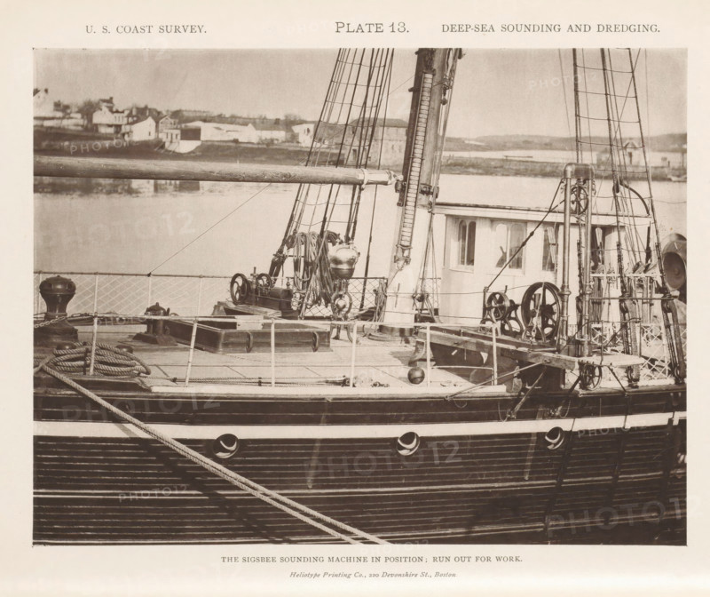 View of the Sigsbee sounding machine on the George S. Blake, page, photomechanical print, inscription: 'The Sigsbee sounding machine in position: run out for work.', name: 'Heliotype Printing Co., 220 Devonshire St., Boston.', number: 'Plate 13.', United States of America, printer (person): Heliotype Printing Company, Boston (Massachusetts), c. 1870 - in or before 1880, printer (person), North America, Massachusetts, paper, collotype, photoprint, height 158 mm x width 208 mm, steamship, motorship, machines, parts of machines, tools and appliances, fathoming, sounding, A sepia-toned photograph showing the deck and side of a wooden ship with visible rigging, masts, coiled ropes, pulleys, winches, and metal fittings, alongside a small deckhouse with windows and a railing; in the background across the water there are low buildings and shoreline features.