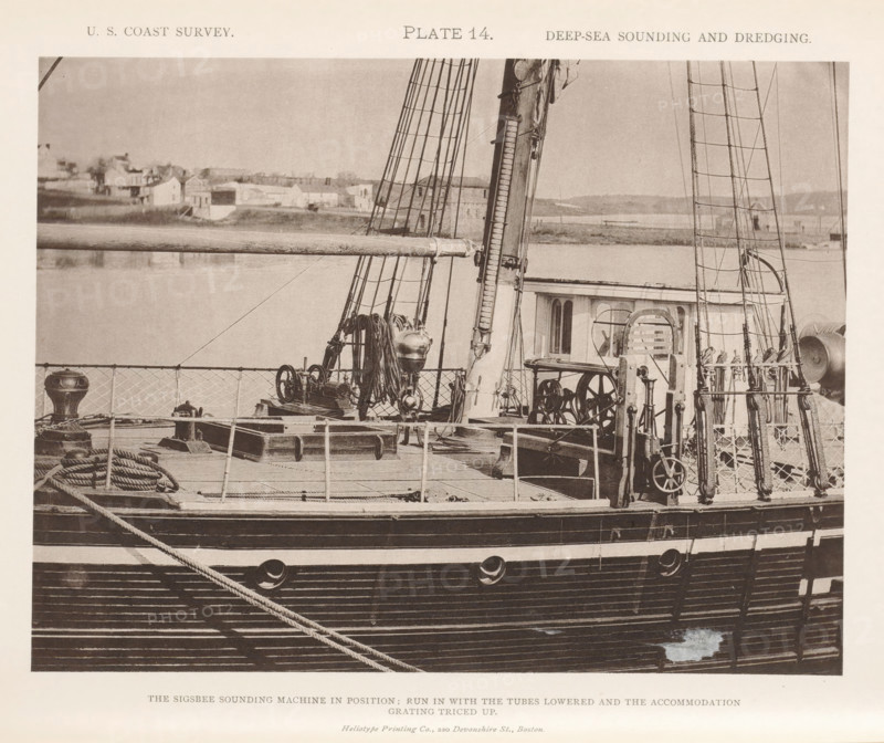 View of the Sigsbee sounding machine on the George S. Blake, page, photomechanical print, name: 'Heliotype Printing Co., 220 Devonshire St., Boston.', inscription: 'The Sigsbee sounding machine in position: run in with the tubes lowered and the accommodation grating triced up.', number: 'Plate 14.', United States of America, printer (person): Heliotype Printing Company, Boston (Massachusetts), c. 1870 - in or before 1880, printer (person), North America, Massachusetts, paper, collotype, photoprint, height 160 mm x width 212 mm, steamship, motorship, machines, parts of machines, tools and appliances, fathoming, sounding, A sepia-toned photograph showing the deck and rigging of a wooden sailing vessel alongside a calm body of water, with a shoreline of buildings and low hills visible in the background. The deck contains coiled ropes, a winch, a mounted drum, various pulleys and mechanical fittings, and sections of lattice railing. Two tall masts with ratlines and standing rigging rise fr...