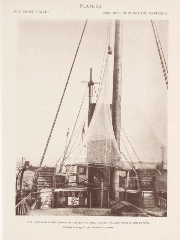View of a trawl on the deck of the George S. Blake, page, photomechanical print, number: 'Plate 28.', inscription: 'The improved trawl shown as having 'tripped' after fouling with rough bottom.', name: 'Heliotype Printing Co., 220 Devonshire St., Boston.', United States of America, printer (person): Heliotype Printing Company, Boston (Massachusetts), c. 1870 - in or before 1880, printer (person), North America, Massachusetts, paper, collotype, photoprint, height 208 mm x width 160 mm, fishing net, ships (in general), A sepia-toned photograph showing the deck and upper structures of a vessel with tall masts, rigging lines, and large nets suspended from the masts; paddle wheels are visible on both sides of the vessel amid stairways and railings, with a cabin structure near the center featuring a round porthole and steps leading down to lower decks; wooden deck planks, coiled ropes, and various winches and pulleys are visible, and a person stands near one of the paddle wheels on the right...