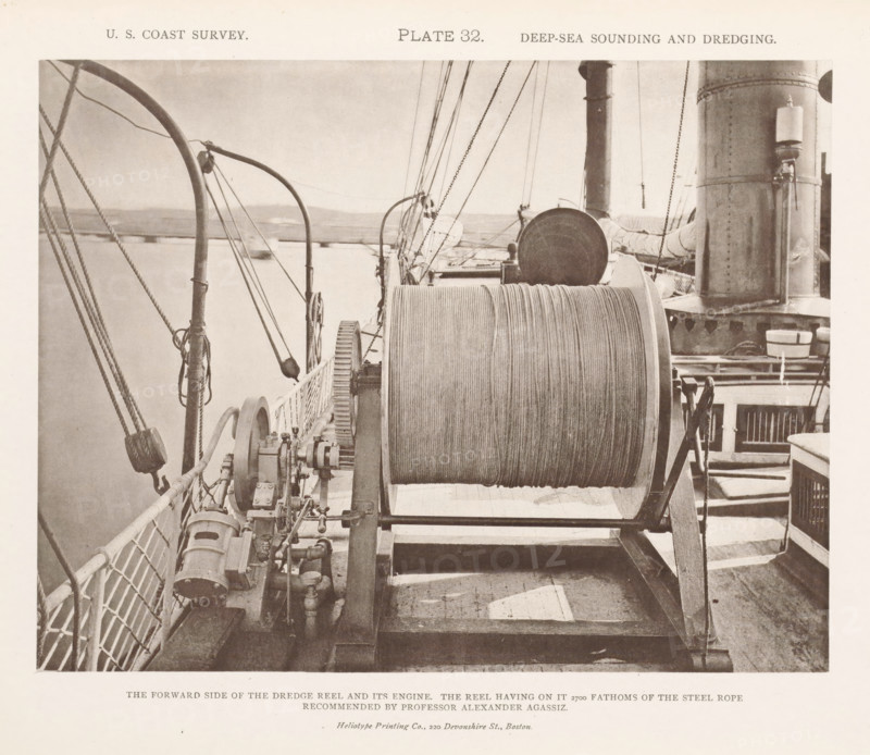Dredge reel on the deck of the George S. Blake, page, photomechanical print, inscription: 'The forward side of the dredge reel and its engine. The reel having on it 2700 fathoms of the steel rope recommended by professor Alexander Agassiz.', name: 'Heliotype Printing Co., 220 Devonshire St., Boston.', number: 'Plate 32.', United States of America, printer (person): Heliotype Printing Company, Boston (Massachusetts), c. 1870 - in or before 1880, printer (person), North America, Massachusetts, paper, collotype, photoprint, height 168 mm x width 218 mm, ships (in general), dredge, dredging machine, A sepia-toned photograph showing a ship's deck with a large horizontal reel of rope mounted on a metal frame in the center foreground, coiled rope visible on the drum; machinery with gears and pipes sits beside the reel toward the left, and a railing with netting runs along the left edge; rigging lines, pulleys, and curved metal stanchions extend upward and diagonally across the scene; toward t...