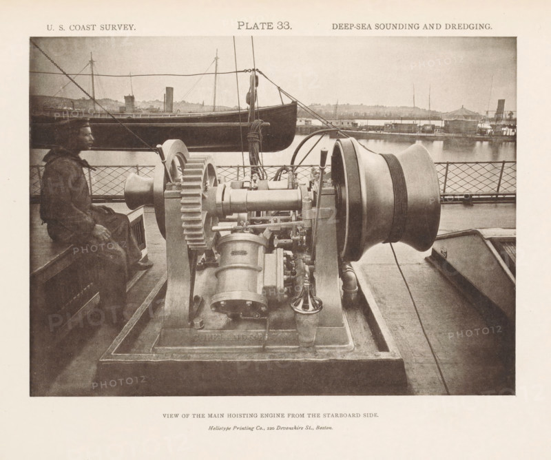 Hoisting engine on the deck of the George S. Blake, page, photomechanical print, name: 'Heliotype Printing Co., 220 Devonshire St., Boston.', inscription: 'View of the main hoisting engine from the starboard side.', number: 'Plate 33.', United States of America, printer (person): Heliotype Printing Company, Boston (Massachusetts), c. 1870 - in or before 1880, printer (person), North America, Massachusetts, paper, collotype, photoprint, height 153 mm x width 209 mm, drawing, pulling something, ships (in general), machines, engines, crafts and industries, A sepia-toned photograph showing a ship deck with a large mechanical hoisting device in the foreground, featuring visible gears, a cylindrical drum with coiled cable, pipes, bolts, and metal fittings; a man in work clothes and a cap sits to the left on a bench facing right; behind the machinery a lifeboat is suspended above the water, with ropes and rigging extending upward; a railing with a diamond-patterned metal mesh runs along the e...