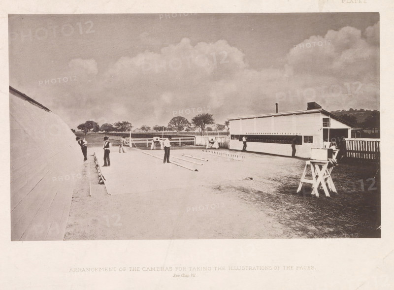 The Horse in Motion, as Shown by Instantaneous Photography, The horse in motion as shown by instantaneous photography with a study on animal mechanics based on anatomy and the revelations of the camera in which is demonstrated the theory of quadrupedal locomotion, book, writer (clerical worker): JDB Stillman, publisher: James R. Osgood & Company, Boston (Massachusetts), 1882, writer (clerical worker), North America, Massachusetts, textile materials, pasteboard, paper, linen (material), photoaquatint, lithography, printing, height 314 mm x width 246 mm x thickness 50 mm, A sepia-toned outdoor scene shows a wide open area with a long low building on the right that has small windows and a raised roof section, a tall narrow fence extending from it, and a wooden stand with a box-like object in the foreground near the building. Several men wearing hats and dark trousers are scattered across the ground, some standing and some leaning, with long narrow planks laid out on the surface between th...