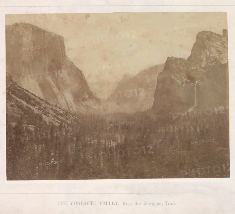 The Yosemite Valley, from the Mariposa Trail, View of the Yosemite Valley, photograph, page, number: 'I.', photographer: Carleton E. Watkins, Yosemite Valley, c. 1860 - in or before 1868, North America, California, paper, albumen print, height 155 mm x width 205 mm, mountains, dale, valley, A sepia-toned landscape photograph showing a wide valley framed by steep rock cliffs and rounded granite formations, with a dense forest of coniferous trees filling the valley floor. One tall cliff on the left rises nearly vertically with striated rock faces and a sloping base, while opposite on the right there are layered rocky outcrops and a narrow waterfall cascading down a dark rock face. Mist or low clouds hang between the distant ridges, softening the outlines of the mountains, and the image has a faded, aged appearance with light mottling and uneven tonality across the sky and rock surfaces.
